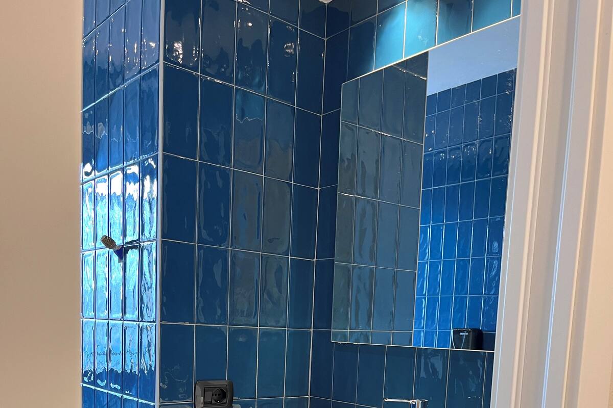 A bathroom with blue tiles, a white sink, and a wooden shelf.