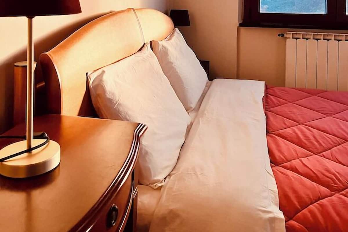 A hotel room with a bed, a bedside table with a lamp, and a window with a view of the mountains.