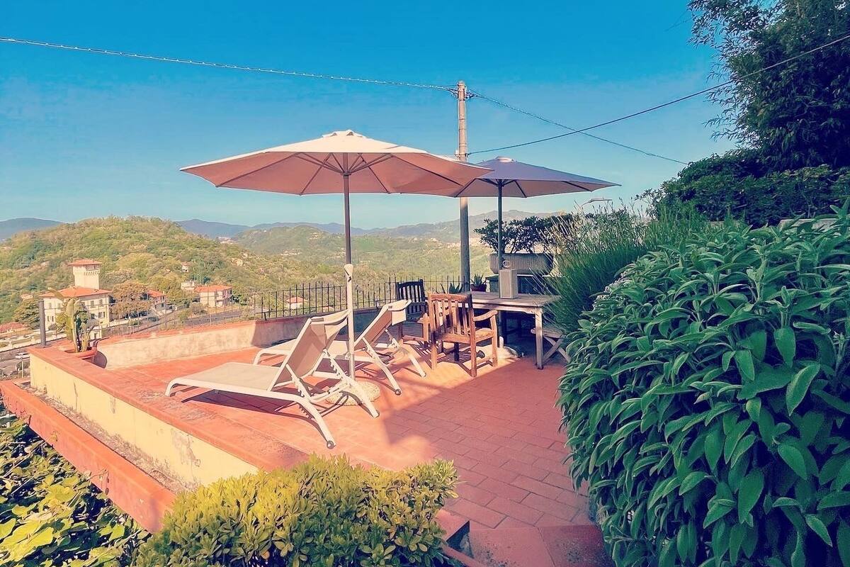 A rooftop terrace with outdoor seating, a view of the surrounding landscape, and a clear sky.