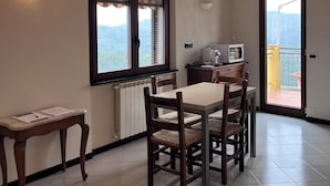 A dining area with a table and chairs, a window with blinds, a radiator, and a view of a balcony. - Collimare rooms (Vezzano Ligure)