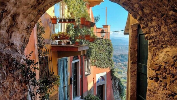 A narrow stone pathway leading to a building with a balcony adorned with potted plants. - Collimare rooms (Vezzano Ligure)