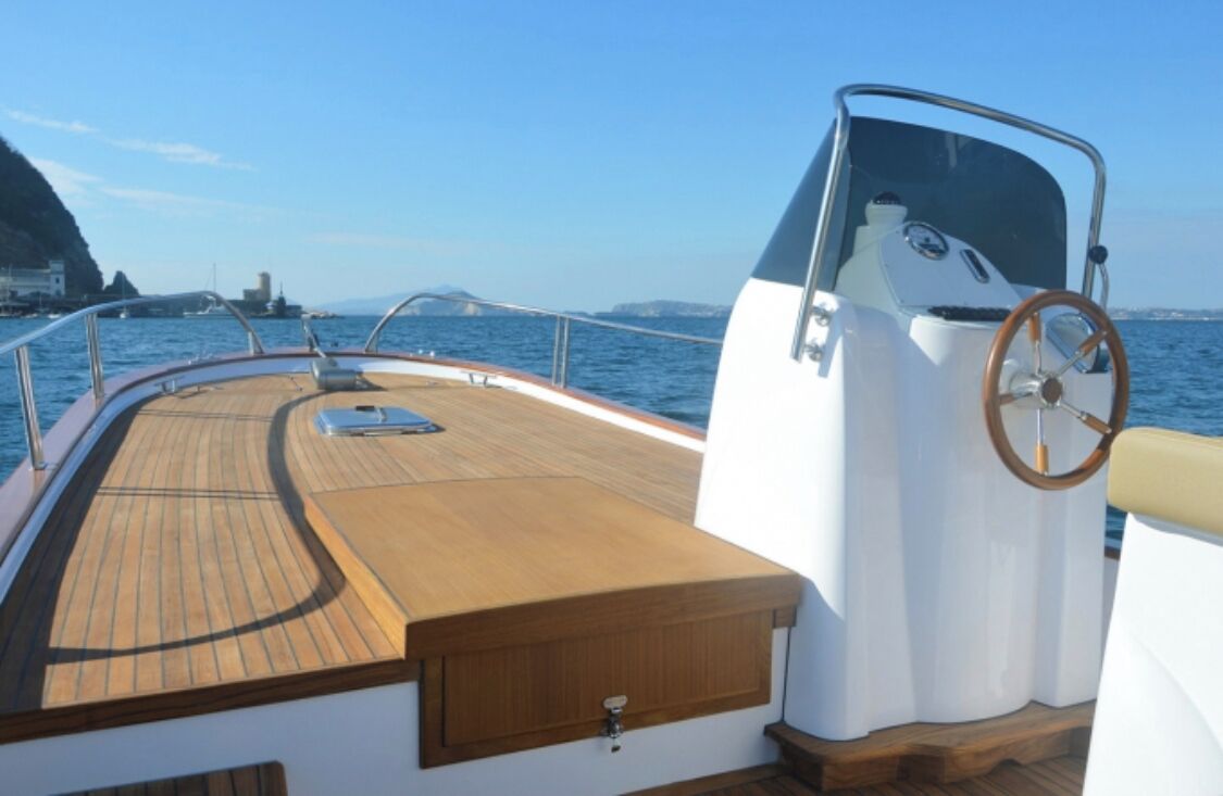 Cubierta de barco con suelo de madera, timón y barandilla de metal.