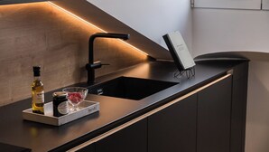 A modern kitchen with a black countertop, a stainless steel sink, and a tray holding a bottle, jar, and glass.