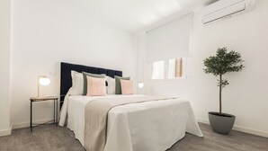 Une chambre à coucher avec un lit, des tables de chevet, une plante en pot et une fenêtre.