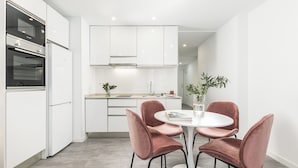 Une cuisine moderne avec des meubles blancs, un four double et une table de salle à manger ronde, accompagnée de quatre chaises.