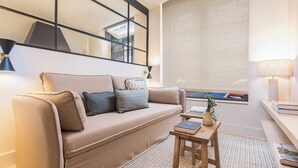 Ett modernt vardagsrum med en beige soffa, ett litet träbord och ett fönster med utsikt.