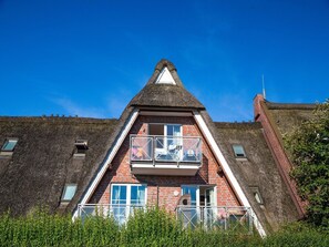 A building with a triangular roof, a balcony with glass railings, and a brick facade. - Apartment 'Fokuhl' with Shared Garden, Balcony and Wi-Fi (Hooksiel)