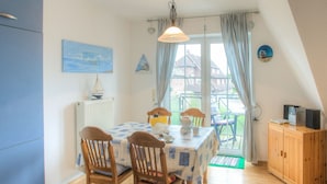 A dining area with a table, chairs, a radiator, a window with curtains, and a view of the outside. - Fokuhl Apartment with Shared Garden, Balcony, and Wi-Fi (Hooksiel)