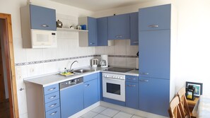 Eine kleine Küche mit blauen Schränken, einer weißen Arbeitsplatte, einer eingebauten Mikrowelle, einer Kaffeemaschine und einem Herd.