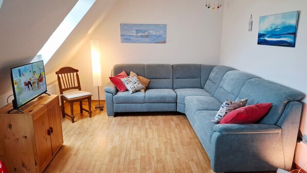 Un salon chaleureux avec un meuble en bois, un canapé gris, une chaise en bois et un téléviseur posé sur un meuble.