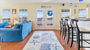 A living room with a blue sofa, a kitchen with bar stools, and a view through a glass door. - Colorado Riverfront Oasis – Fishing, Views & Perfect Family Getaway (Matagorda)