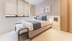 Ein modernes Schlafzimmer mit einem Bett, Nachttischen, einer Bank und einem Fenster mit Jalousien.