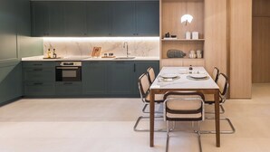 Eine moderne Küche mit dunkelgrünen Schränken, einer Marmorarbeitsplatte und einem Essbereich mit einem Holztisch und Korbstühlen.