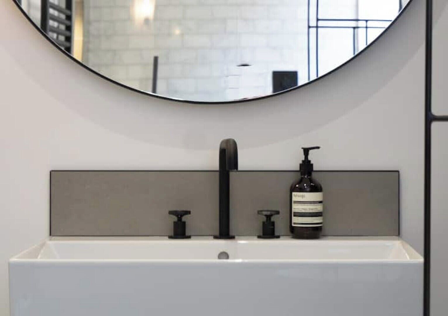 A modern bathroom with a white sink, black faucet, and a bottle of shampoo.