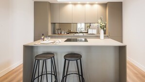 Una cocina moderna con una isla central, dos taburetes de bar y un gran ventanal que proporciona luz natural.