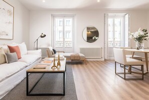 Een moderne woonkamer met een witte bank, een salontafel, een ronde spiegel en een eethoek met een stoel en een tafel.