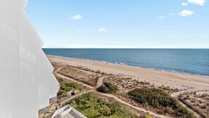 Une vue sur la plage depuis un immeuble à la façade blanche, avec une plage de sable et un ciel dégagé.