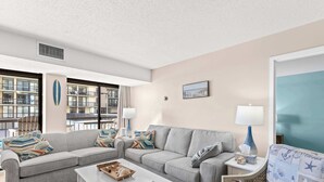 Un soggiorno moderno con un divano grigio, un tavolino da caffè bianco e una poltrona a fantasia. Due lampade su mensole laterali e una finestra con vista sull'esterno dell'edificio.