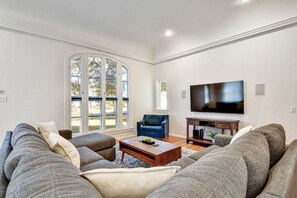 A living room with a large sectional sofa, a blue armchair, a coffee table, and a flat-screen TV mounted on the wall. - San Antonio Resort Home | Pool, Hot Tub, Casita & Game Room (San Antonio)