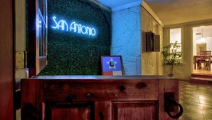 Vastaanottotiski, jonka yläpuolella on neonvalomainos, jossa lukee ”SAN ANTONIO”, ja seinällä on lippu.