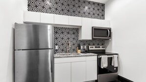 A compact kitchen with a stainless steel refrigerator, microwave, and oven, white cabinets, and a patterned backsplash.