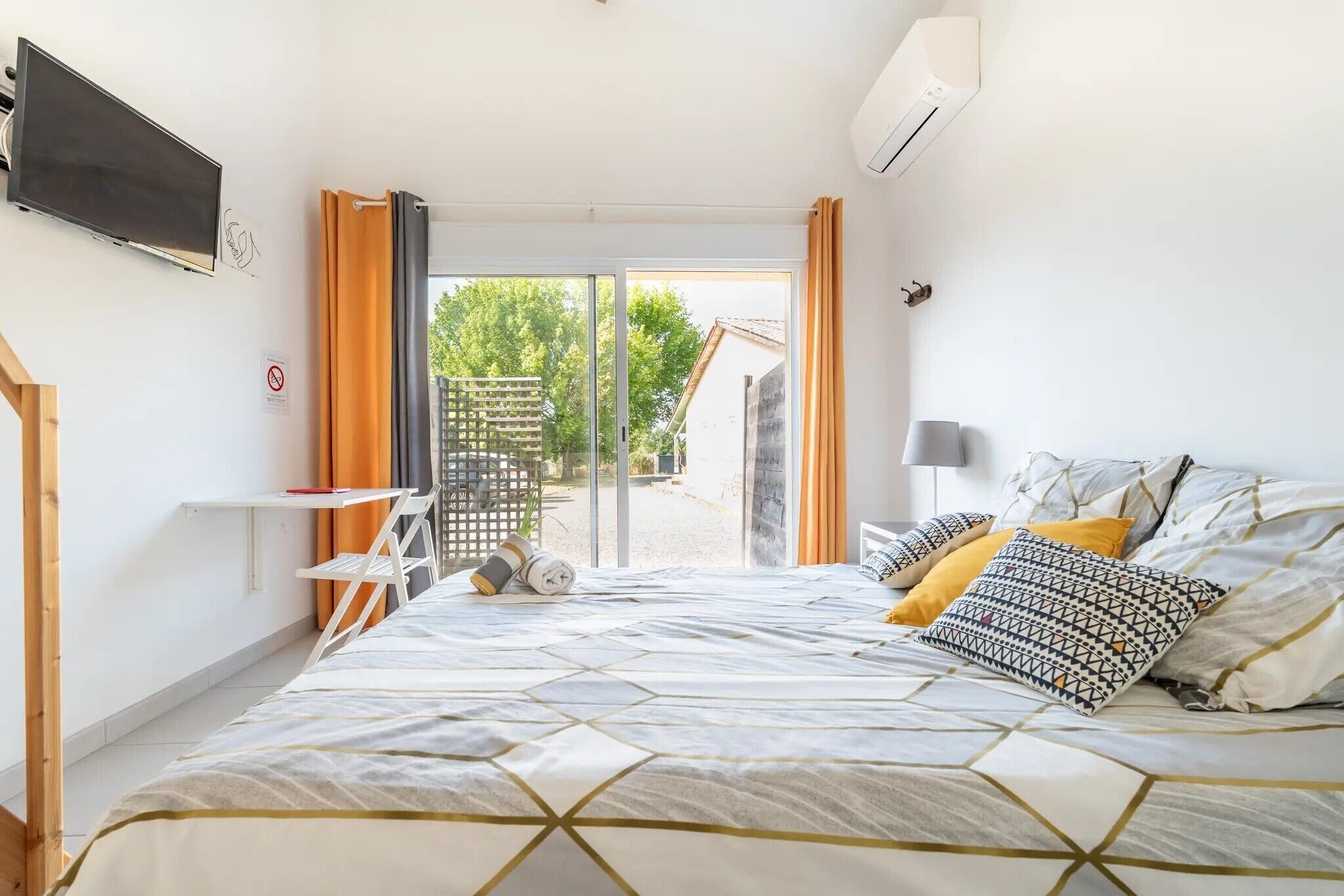 Quarto com cama, escrivaninha, cadeira e ar condicionado.