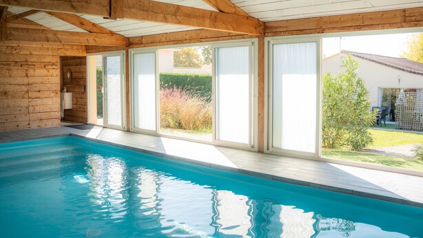 Ein Hallenbad mit Holzbalken, großen Fenstern und Blick ins Freie.