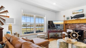 A living room with a leather sofa, a television, a fireplace, and a view of the outdoors. - Cove House with Private Pool, Ocean Views, Family (Owls Head)