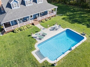 Una casa con piscina, un porche cubierto y un césped.