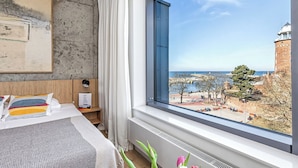 A hotel room with a large window offering a view of a historic building and a body of water. - BalticON Apartments Morska (Kolobrzeg)