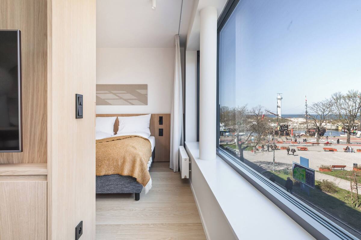 A hotel room with a bed, a large window, and a view of an outdoor area with benches and a map sign.