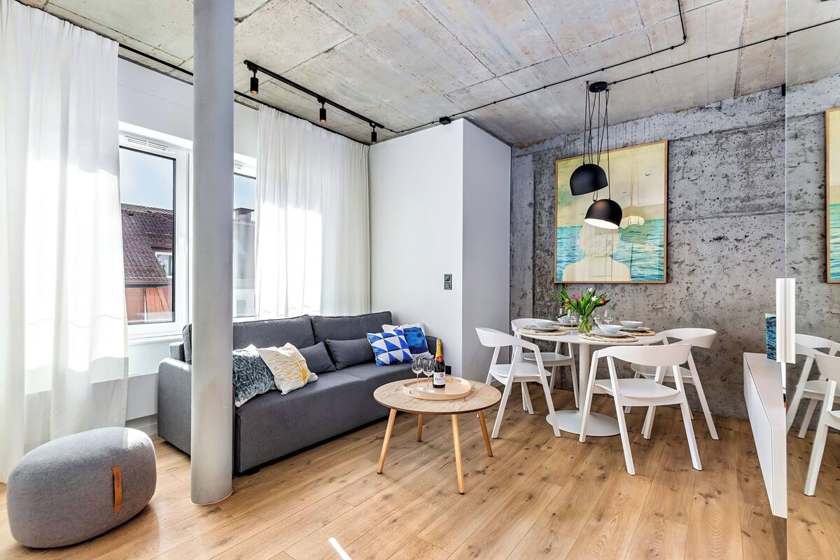 A modern living room with a grey sofa, a round wooden table, and white chairs.