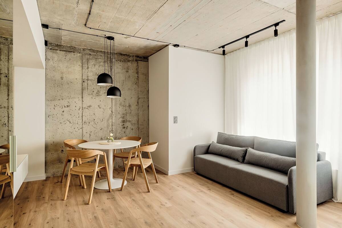 A modern living space with a dining area, a gray sofa, and a concrete accent wall.