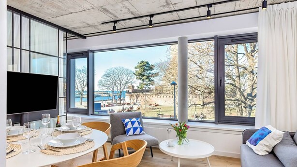 A modern living room with a dining area, large windows, and a view of a park. - BalticON Apartments Morska (Kolobrzeg)