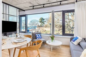 A modern living room with a dining area, large windows, and a view of a park. - BalticON Apartments Morska (Kolobrzeg)