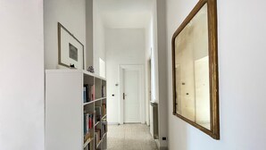 Un couloir étroit avec une bibliothèque blanche, un grand miroir et une porte au fond.