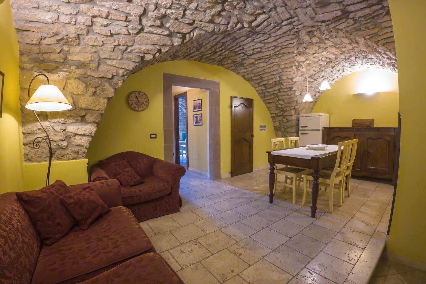 Una habitación acogedora con techo de piedra, un sofá, una mesa de comedor con sillas y un reloj en la pared.