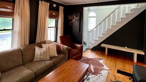 Una sala de estar con un sofá, una mesa de centro de madera, un sillón de cuero y una escalera que sube a un nivel superior.