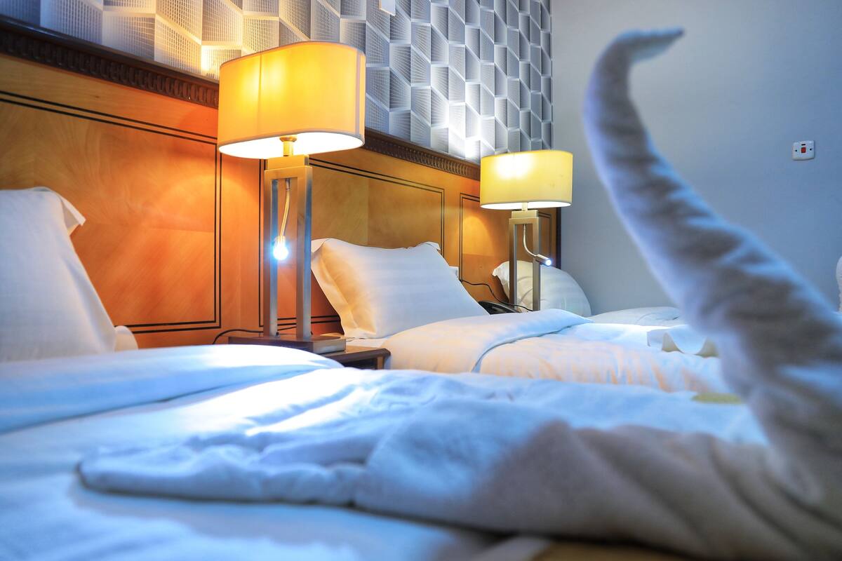 A hotel room with two beds, each with a lamp and a pillow.