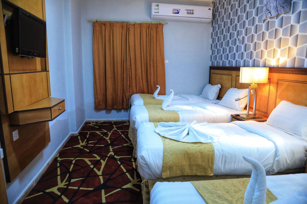 A hotel room with two beds, a TV, an air conditioner, and a patterned carpet.