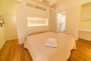 A bedroom with a bed, a bedside table, a wall-mounted light, and a door leading to another room. - Sardinian Gallery Contrada (Bosa)