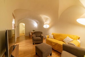 A modern living room with a sofa, armchair, ottoman, and a flat-screen TV. - Sardinian Gallery Contrada (Bosa)