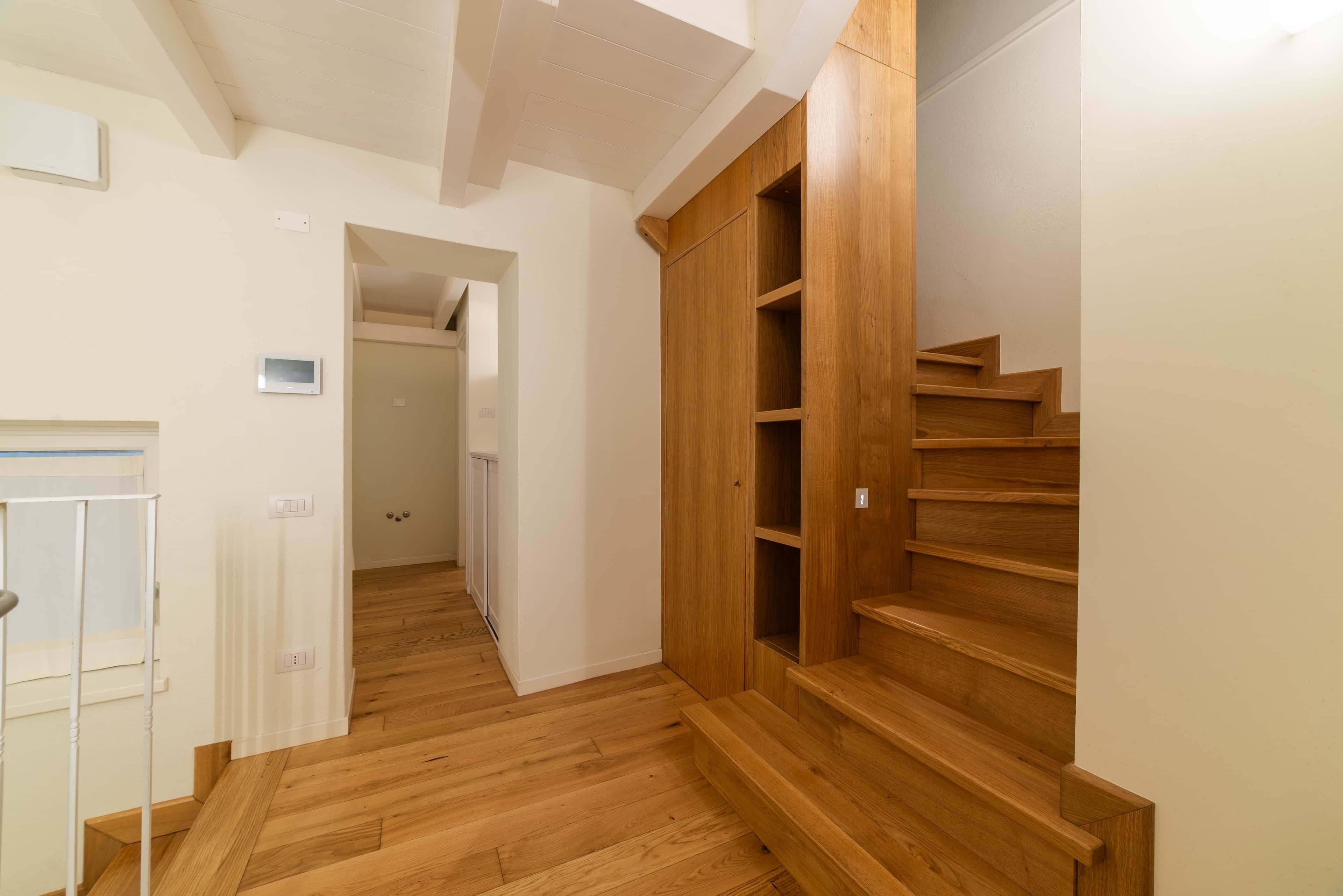 Un couloir doté d’un plancher en bois, d’une porte blanche et d’un escalier en bois avec des étagères intégrées.