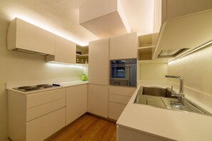 A compact kitchen with white cabinetry, a built-in oven, and a stainless steel sink. - Sardinian Gallery Contrada (Bosa)