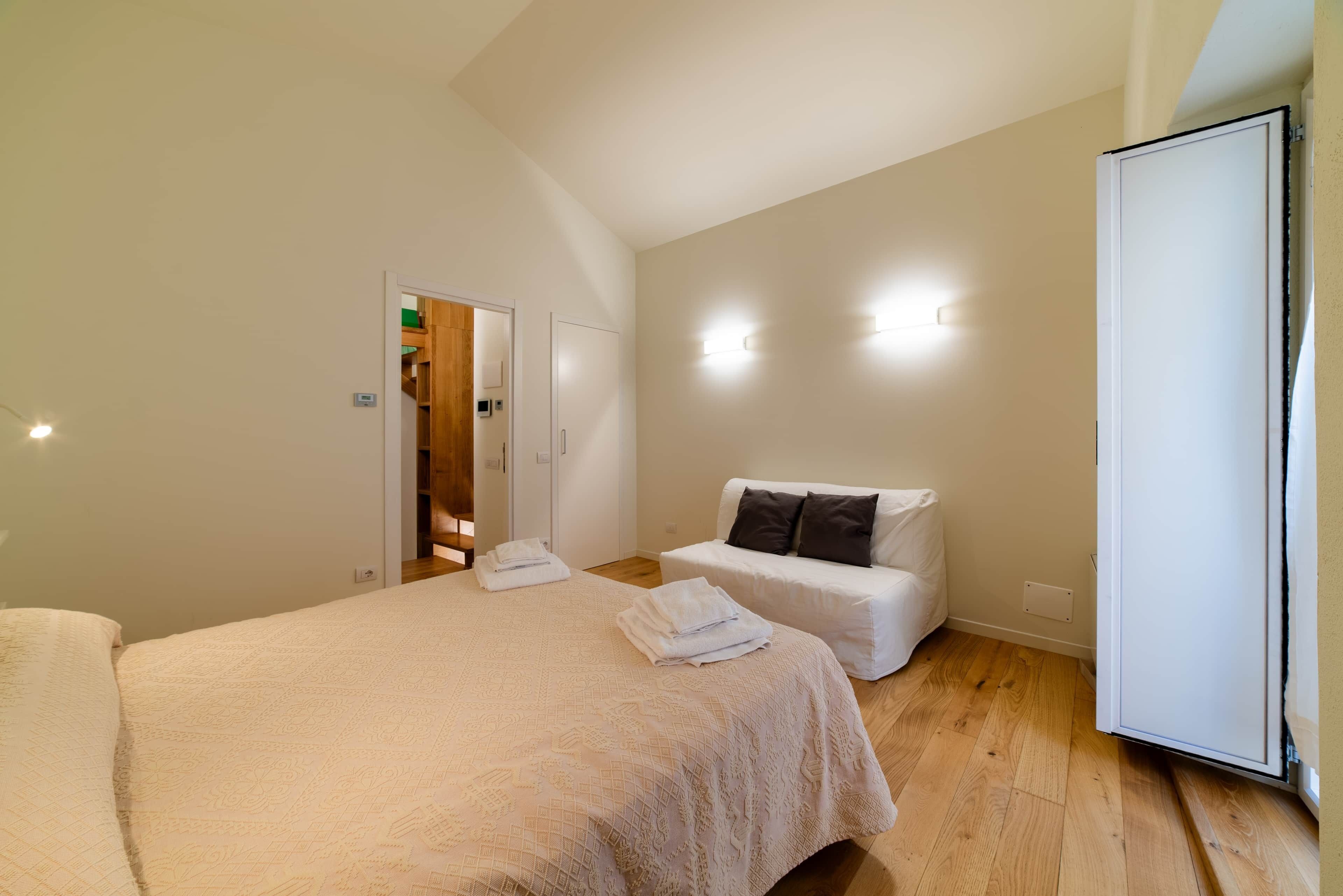 Una camera da letto con un letto grande, un comodino, un divano bianco e un armadio.