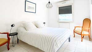 A bedroom with a bed, a chair, a bedside table with a lamp, a framed picture, and a window with blinds. - De Standing Avignon Apartment with Wi-Fi and Air Conditioning (Avignon)