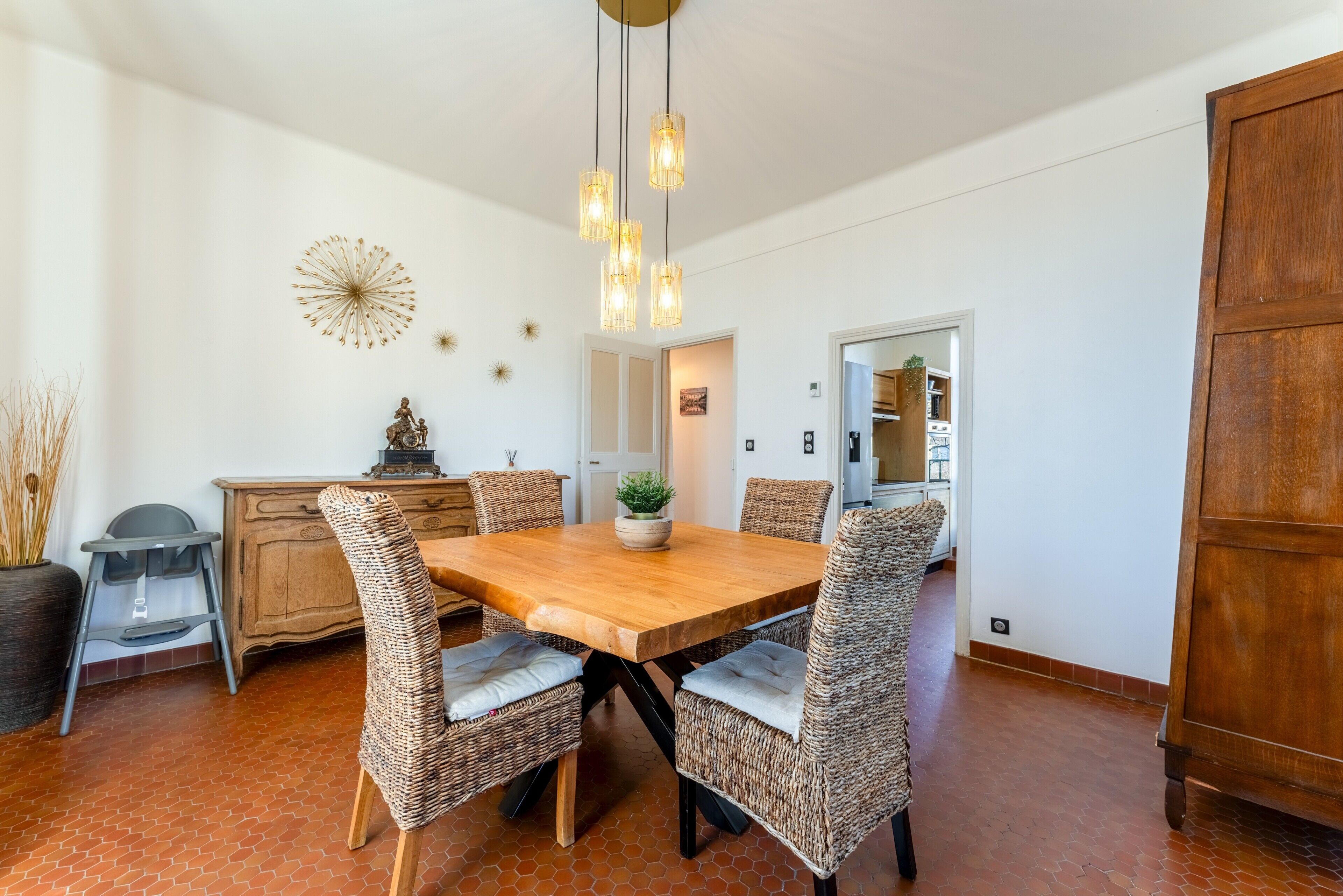 Un espace repas avec une table en bois, des chaises en osier et des luminaires suspendus.