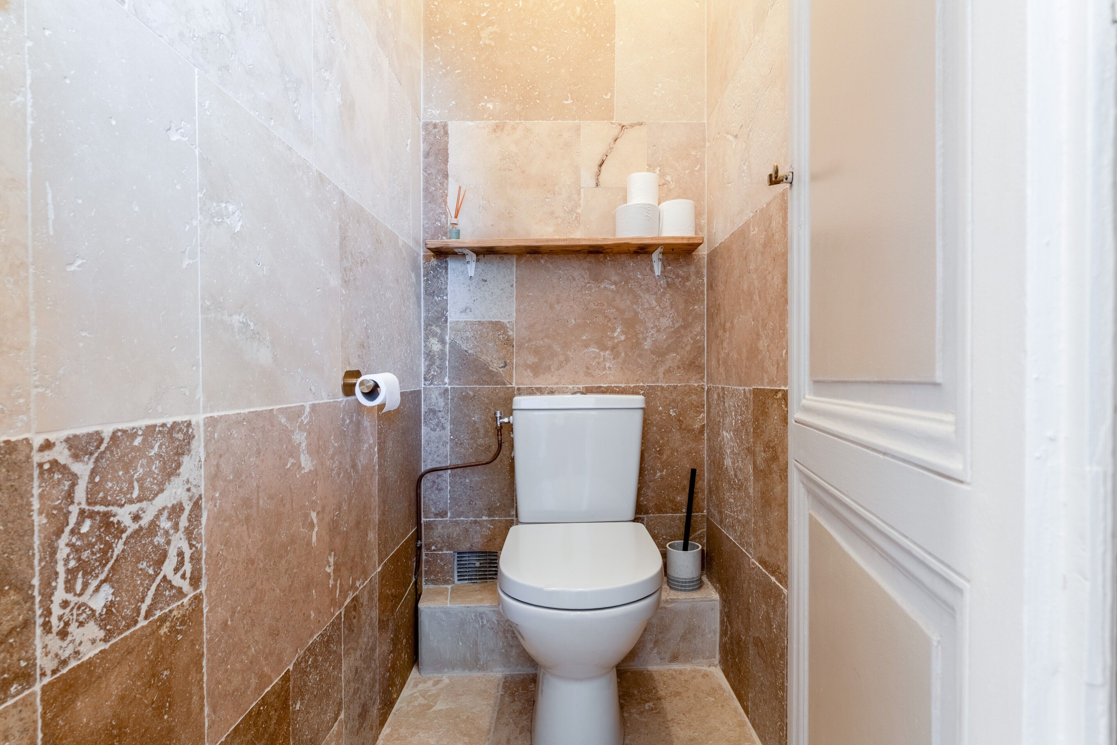 Et badeværelse med toilet, hylde med toiletpapir og en håndtørrer.