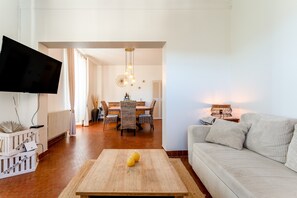 En stue med sofa, sofabord, fjernsyn, spiseplads med bord og stole, samt en lysekrone.