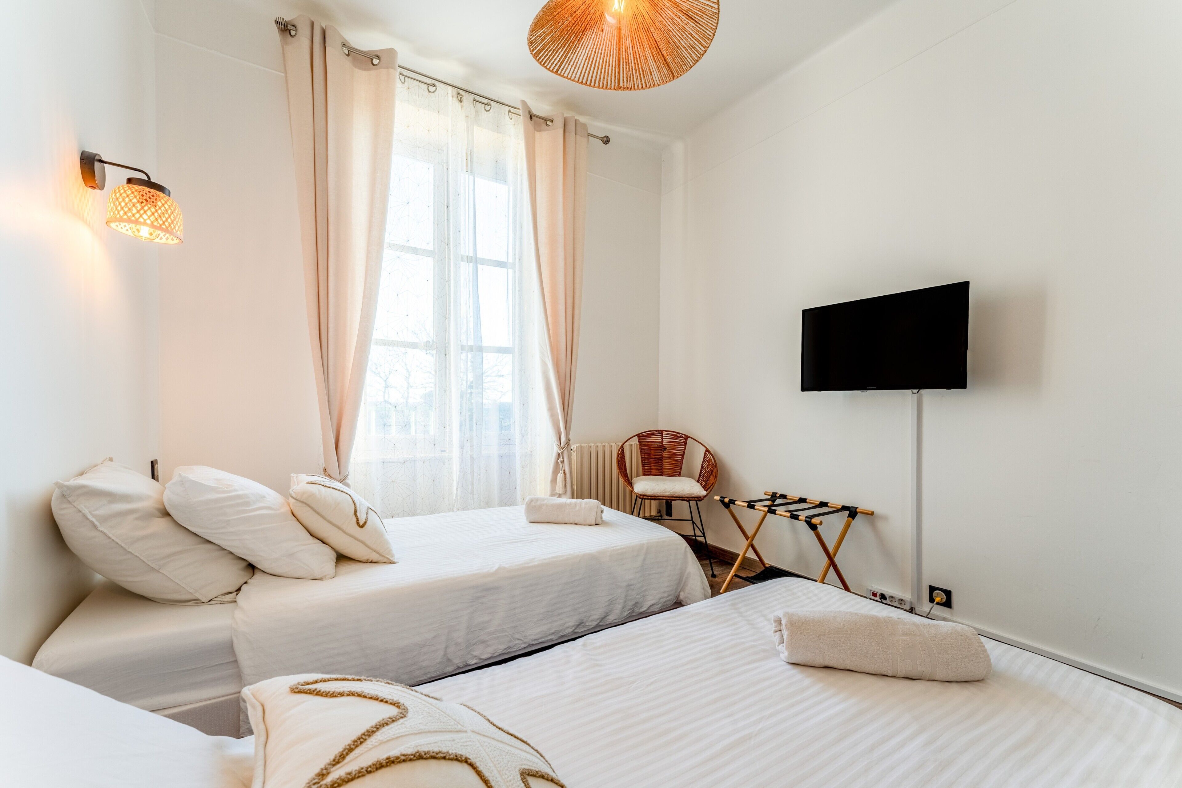 Quarto de hotel com duas camas, televisão, uma cadeira e um varal.